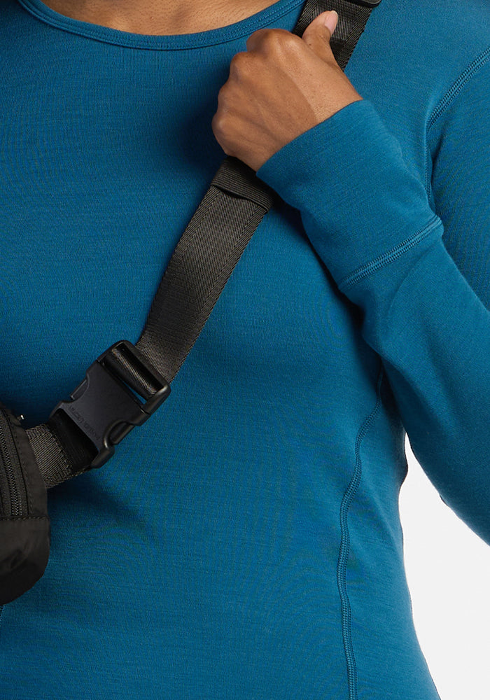 Person in a blue Woolx Hannah Long Sleeve Top holds the black strap of a bag across their shoulder.