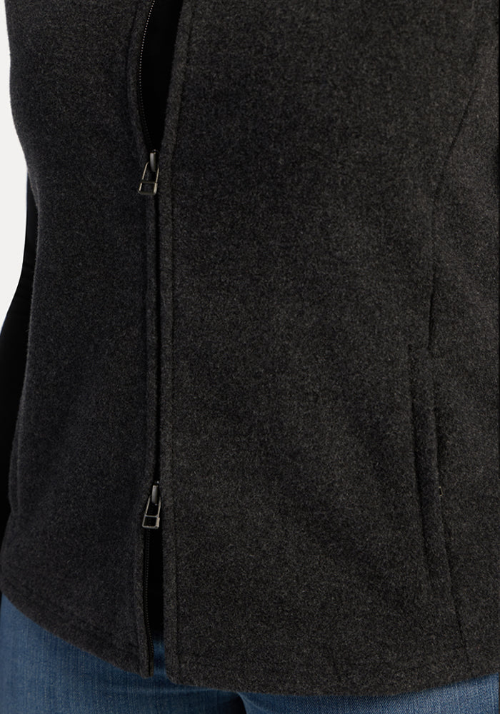A close-up of the Woolx Haley Vest - Carbon Black, layered over blue jeans, highlights its low zipper for style and comfort.