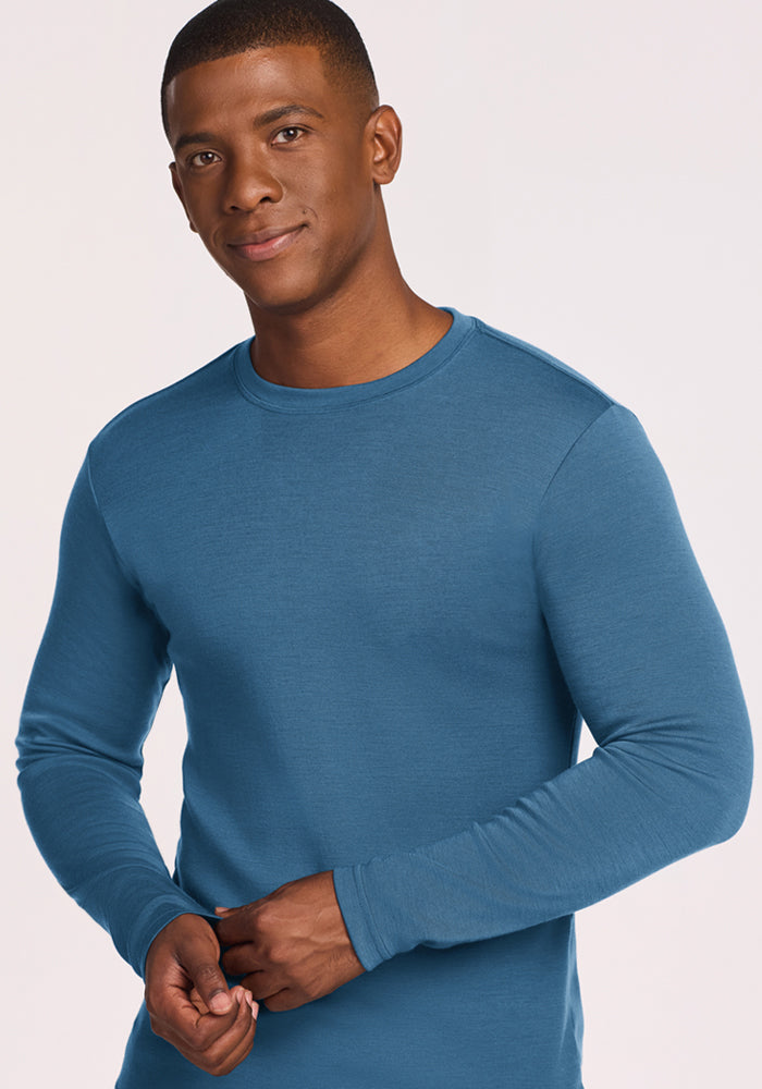 Man in a Woolx Easton Crew Neck Shirt - Blue Ashes smiles gently against a plain, light background.