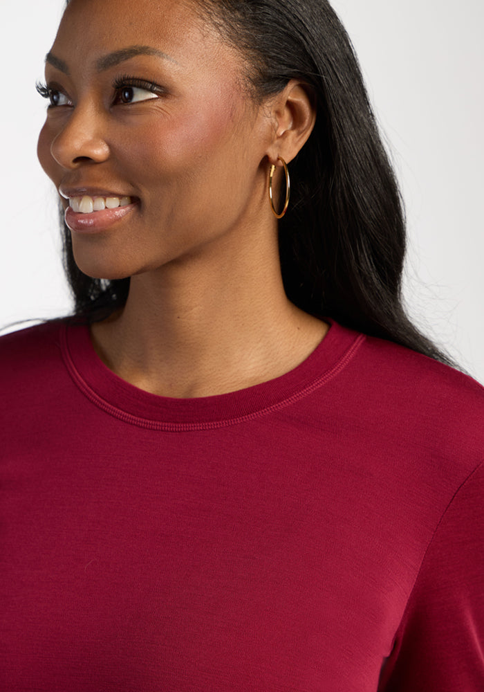Woman smiling in the Woolx Blair Petite Tunic - Beet Red and gold hoops, with long dark hair, on a light background.