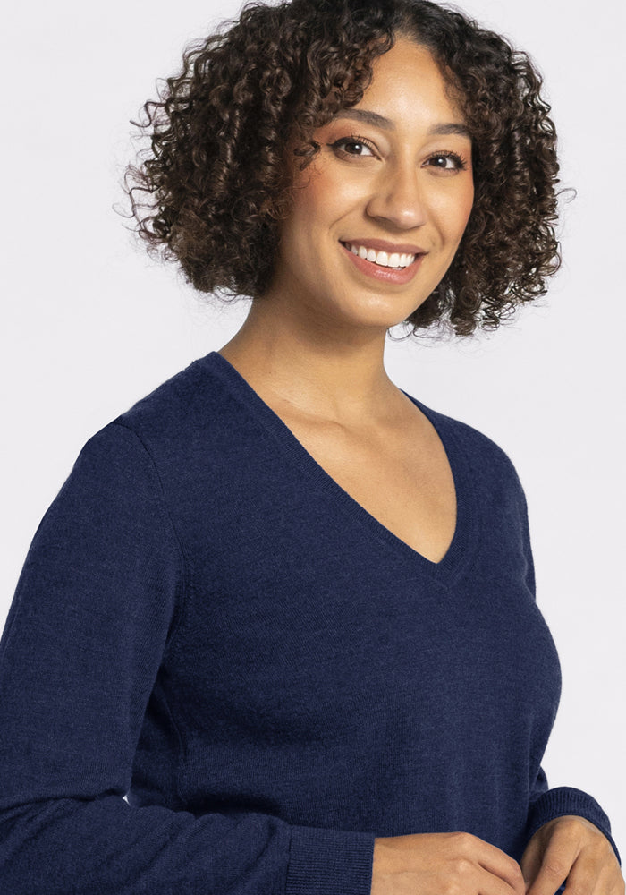 Smiling person with curly hair in a Woolx Francesca Sweater - Ocean Cavern, against a plain light background.