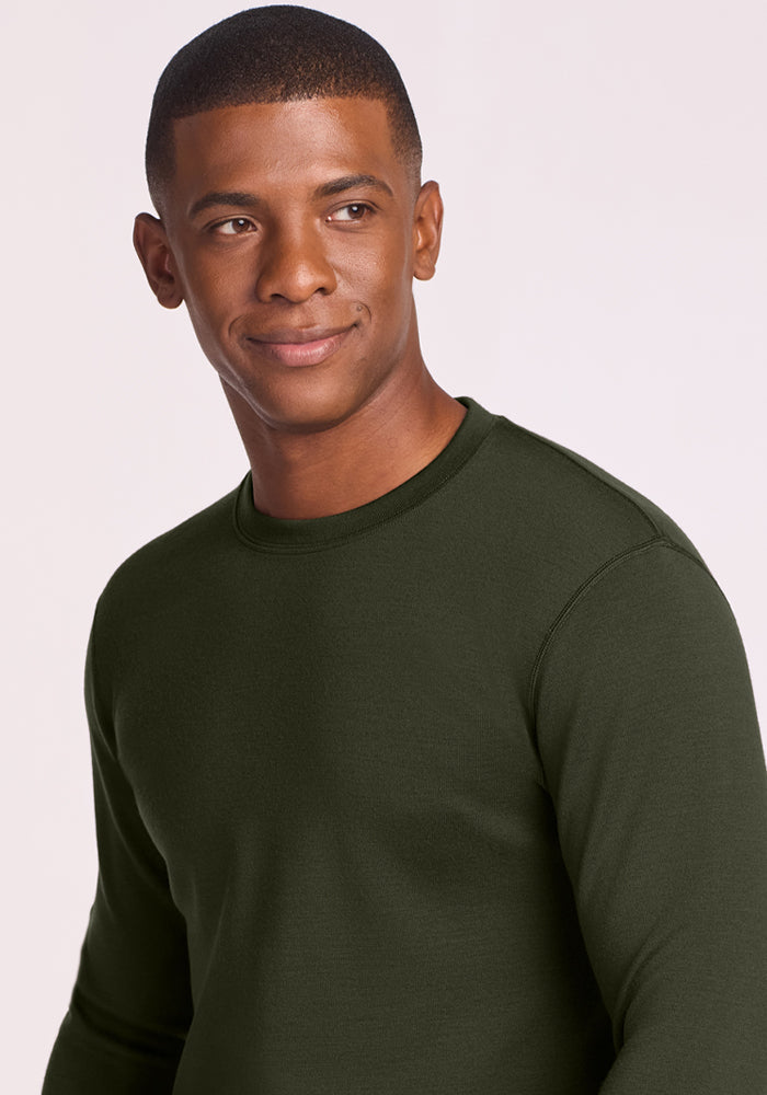 Man wearing Woolx Glacier Long Sleeve Crew in Duffel Bag, looking to the side and smiling against a plain background.