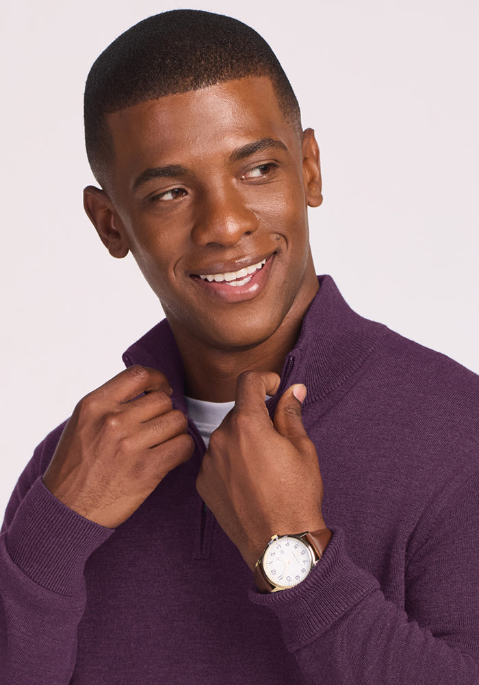 Man wearing Woolx Enzo Quarter Zip in Purple Iris, smiling, looking aside, adjusting collar, and wearing a watch.