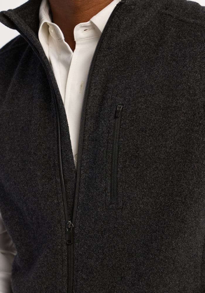 Close-up of a charcoal-colored Woolx Everest Vest - Carbon Black worn over a white collared shirt, with a zippered pocket.