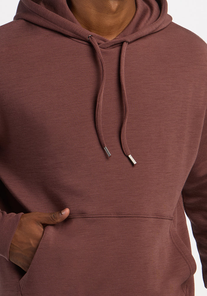 Person wears the Woolx Watson Pullover in Canyon Clay, hand in pocket, highlighting odor resistance and drawstrings.