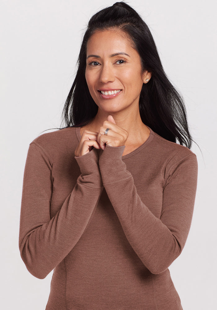 Woman with long dark hair smiles in the Woolx Hannah Long Sleeve Top in Sable Heather, hands near her chin.