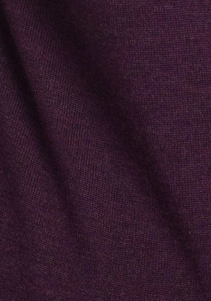 A close-up of the Woolx Francesca Sweater in Deep Plum highlights its dark purple, ribbed fabric with fine texture and weave details, enhanced by subtle diagonal shadows for a travel-friendly look.