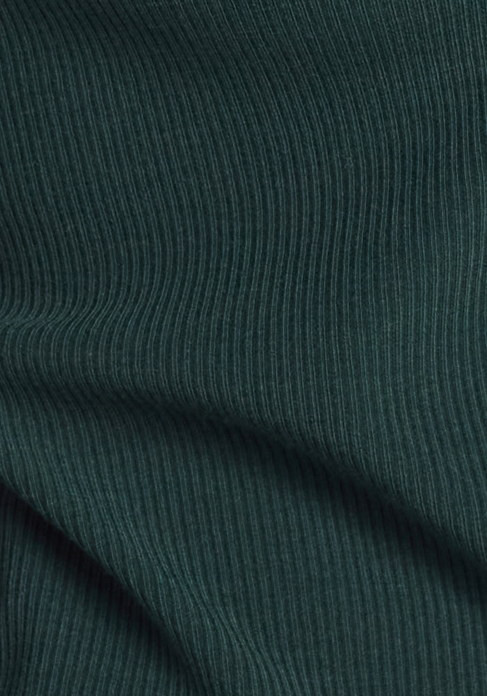 Close-up of the Woolx Caroline Ribbed Twirl Dress in Deep Timber, featuring dark green merino fabric with fine vertical lines—showcasing gentle folds and texture for a stylish, temperature-regulating look suitable for any occasion.