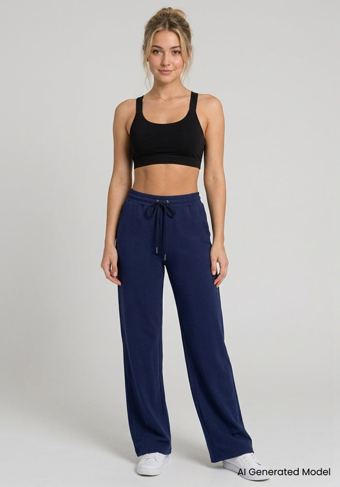 Woman in black sports bra, Woolx Eloise Petite Pants - Ocean Cavern, white sneakers, plain background.