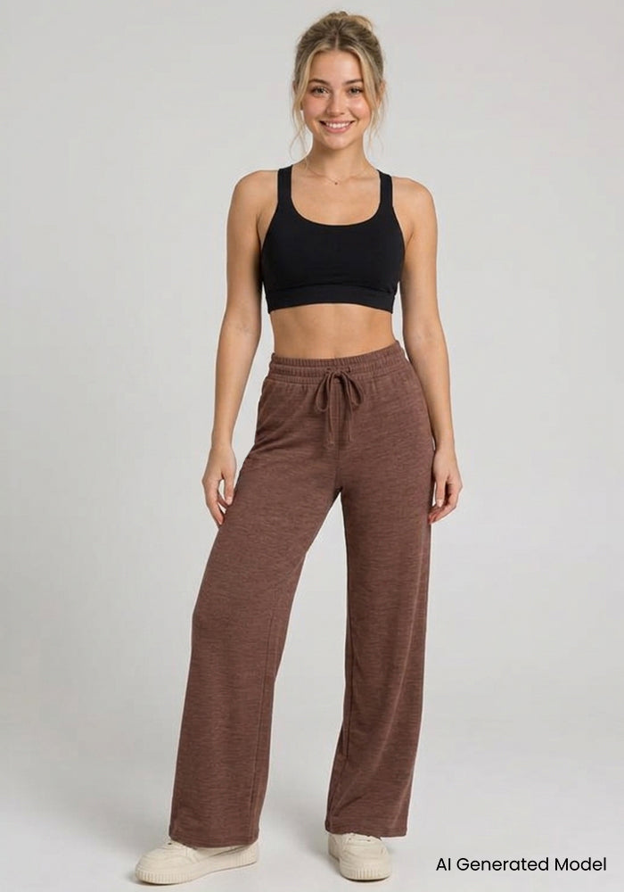Smiling woman wears a black sports bra, Eloise Petite Pants - Sable Heather by Woolx, and white sneakers.