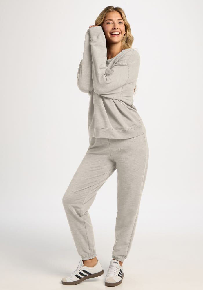 A woman wearing a light gray Woolx Molly Crewneck - Light Ash sweater and matching moisture-wicking jogger pants.