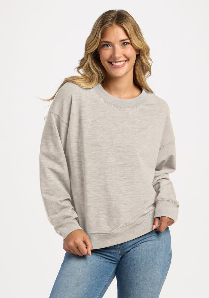 Smiling woman wearing a light gray Woolx Molly Crewneck - Light Ash sweatshirt and blue jeans. 