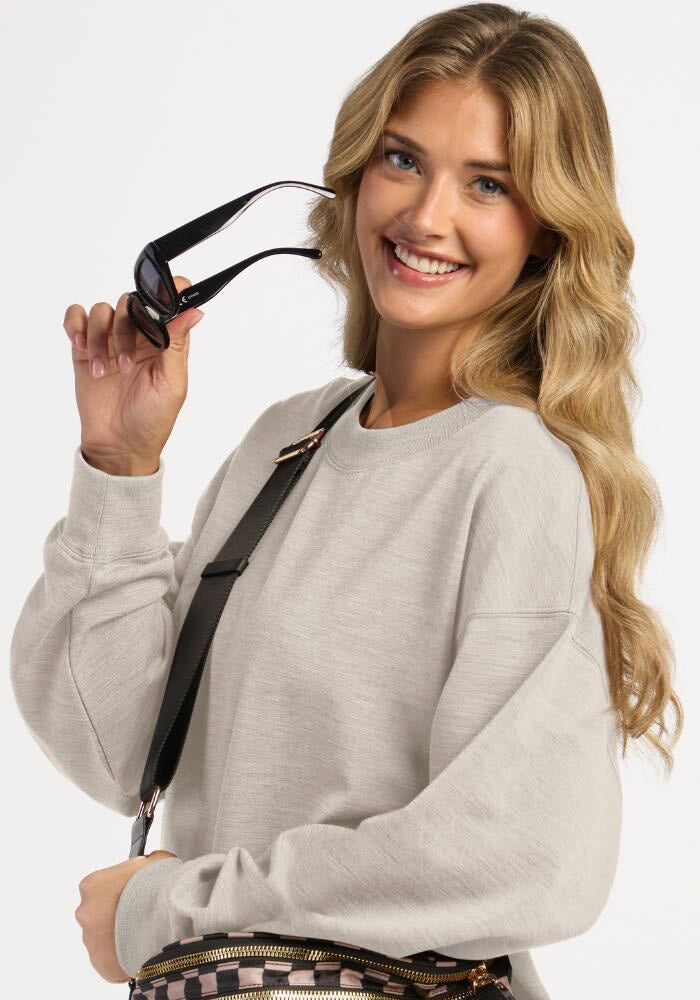 Smiling woman wearing a light ash Woolx Molly Crewneck sweatshirt and holding sunglasses.
