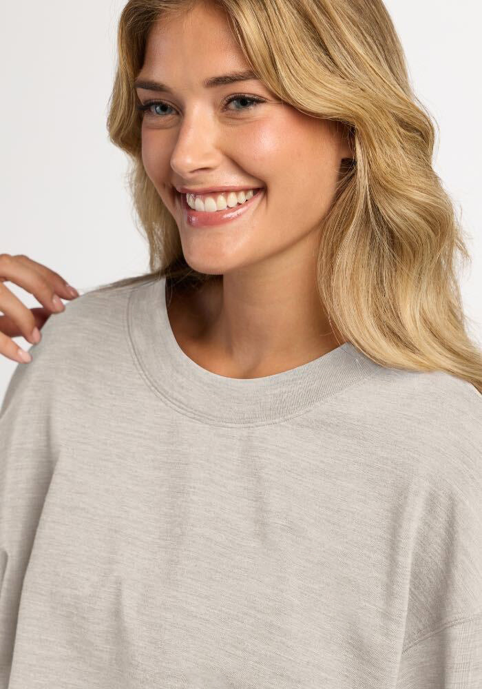 A smiling woman wearing a light ash Woolx Molly Crewneck moisture-wicking merino wool sweater.