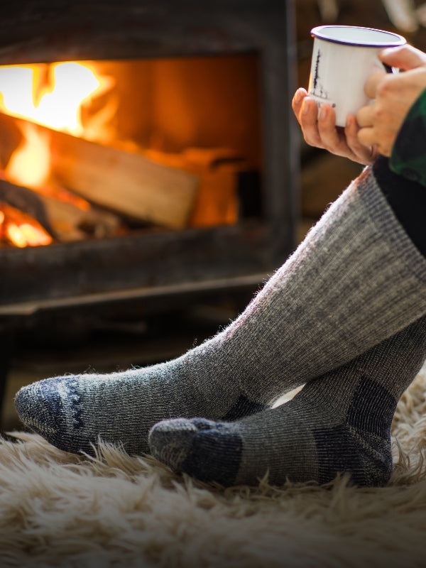 Person sitting in front of a small stove wearing Extreme socks and holding a mug mobile size