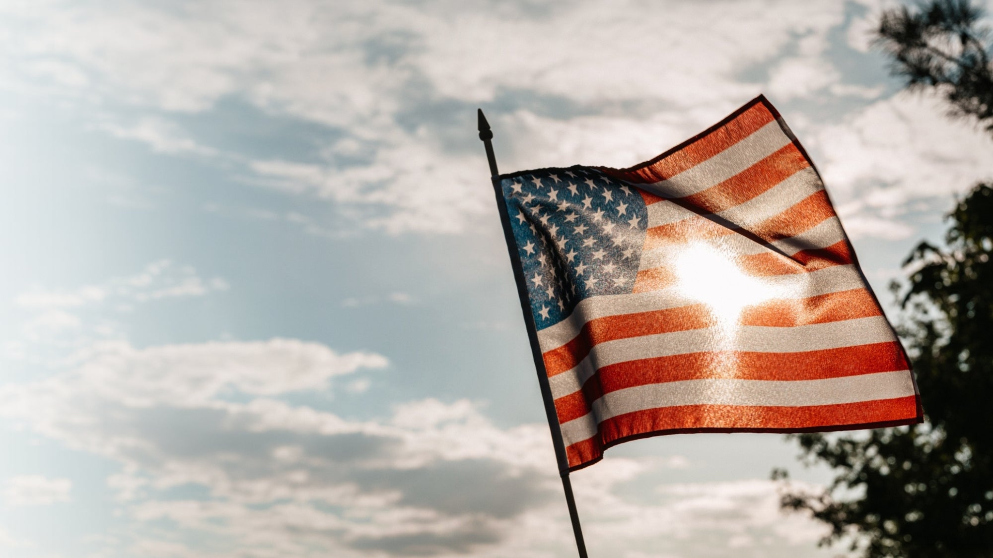 American flag waving against a cloudy sky with sunlight