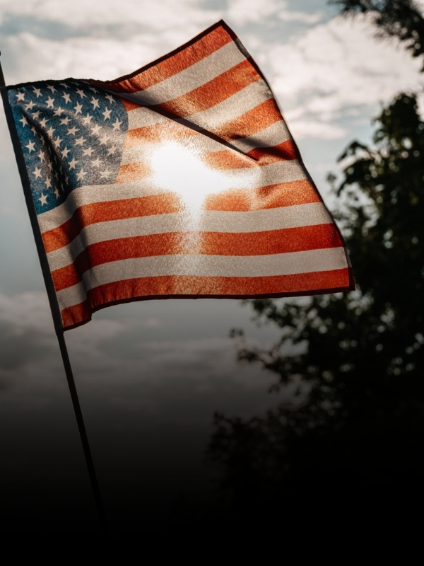 American flag waving against a cloudy sky with trees in the background