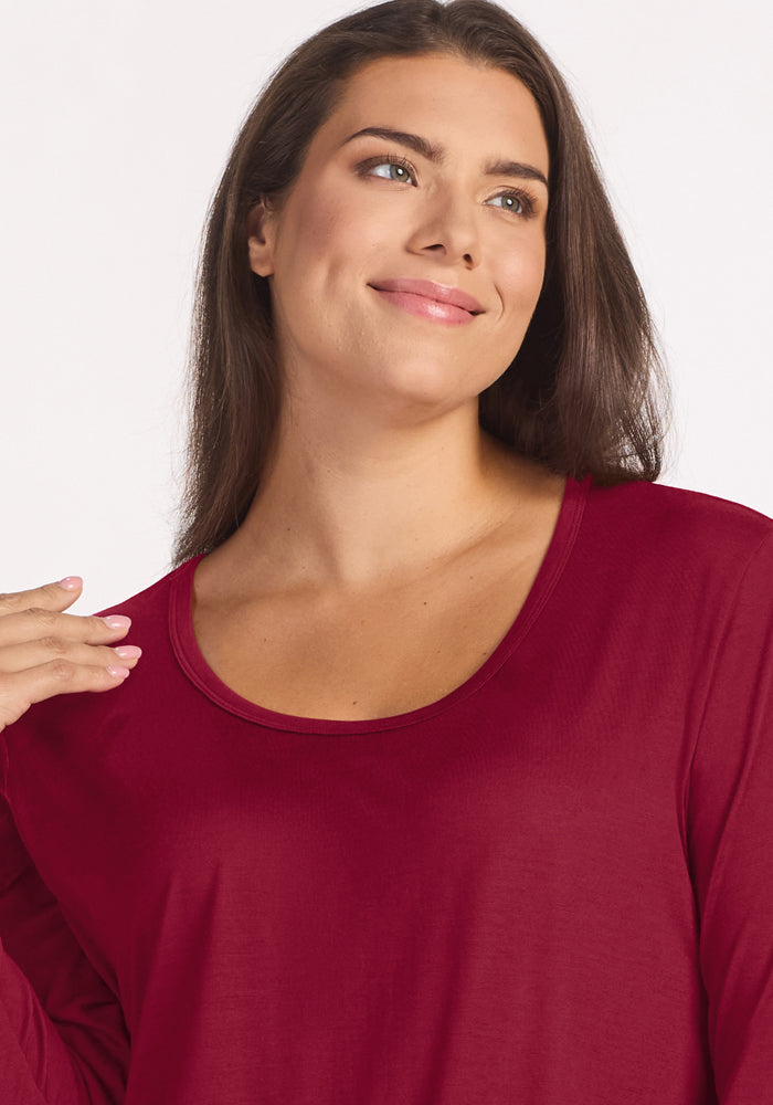 A woman wearing a temperature-regulating, beet red Lucille Long Sleeve Nightgown with a scoop neckline.