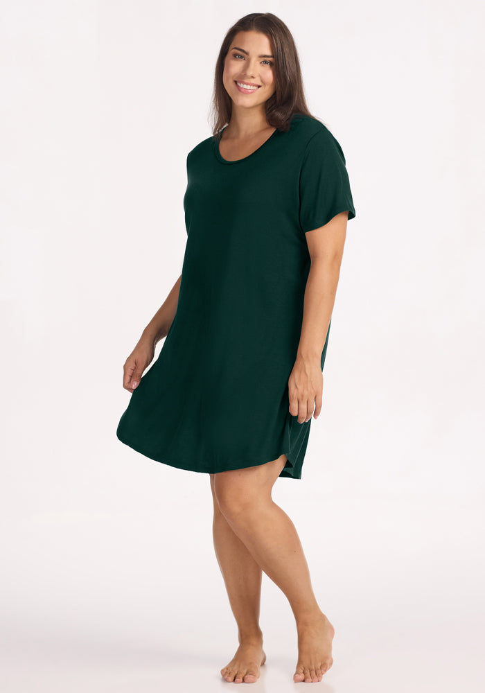 A woman smiles wearing a Deep Pine Woolx Desi Nightgown made of dark green, moisture-wicking merino wool. 