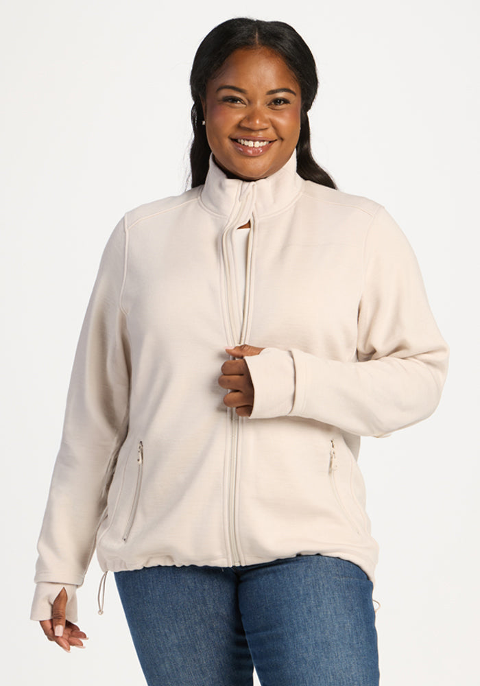 Smiling woman wearing an ecru Woolx Teddy Sweatshirt, a moisture-wicking fleece jacket with thumb holes and zip pockets. 
