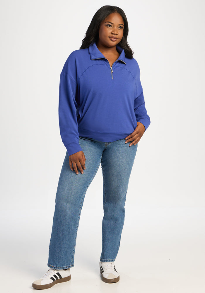 A person wearing a Woolx Tori 1/4 Zip - Royal Blue merino pullover, blue jeans, and sneakers.