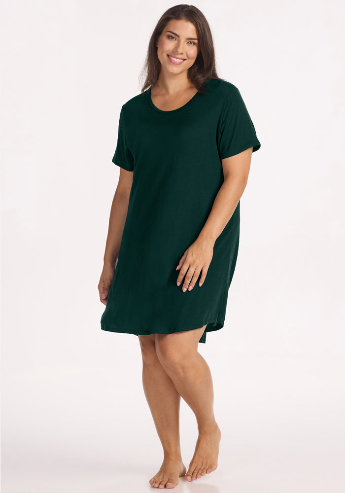A person wears a short-sleeved, dark green, moisture-wicking knee-length Woolx Desi Nightgown - Deep Pine.