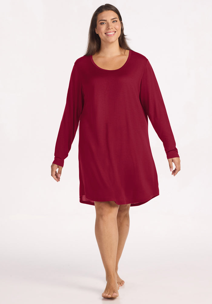 A woman wears a beet red Woolx Lucille Long Sleeve Nightgown, a temperature-regulating, knee-length style.