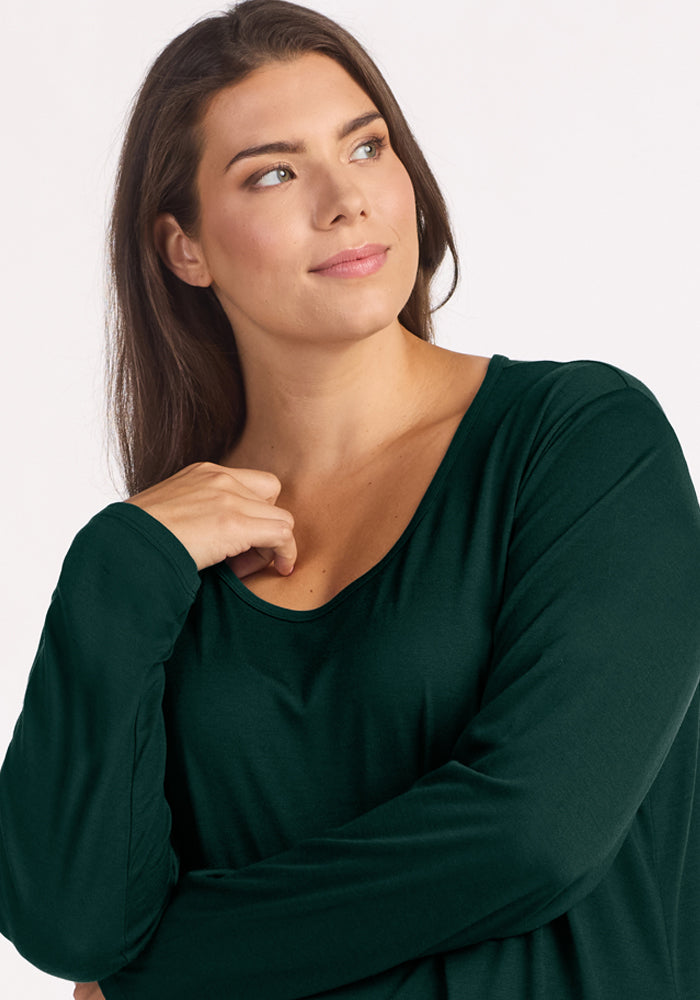 A woman wearing a dark green, long-sleeved Woolx Lucille Long Sleeve Nightgown - Deep Pine with a scoop neckline.