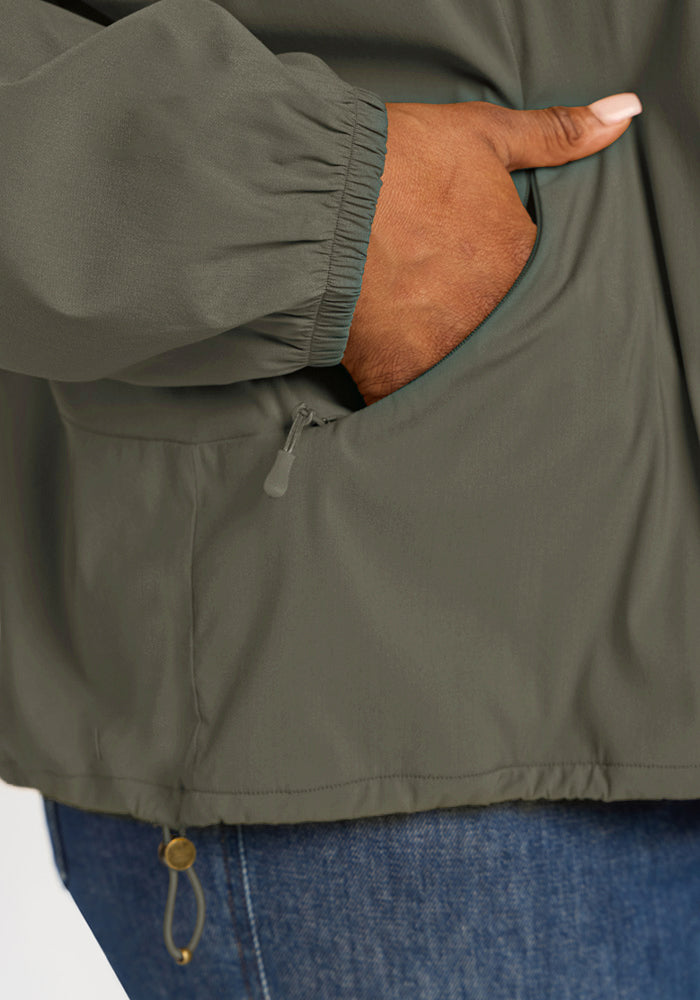 Close-up of a hand in the zippered pocket of a Sage Olive Cooper Windbreaker.