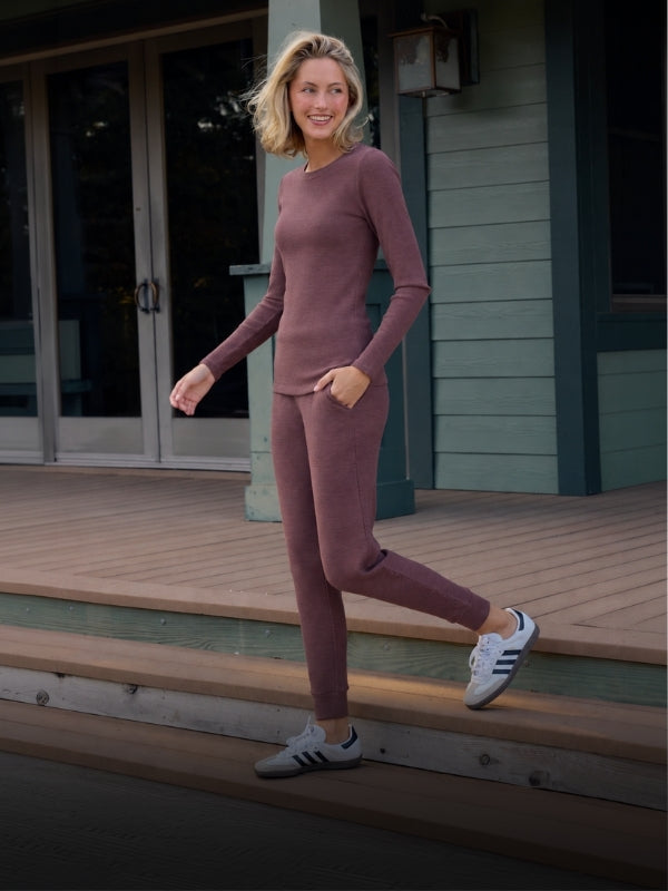 Woman stepping down wooden stairs wearing a maroon ribbed wool set of shirt and pants.