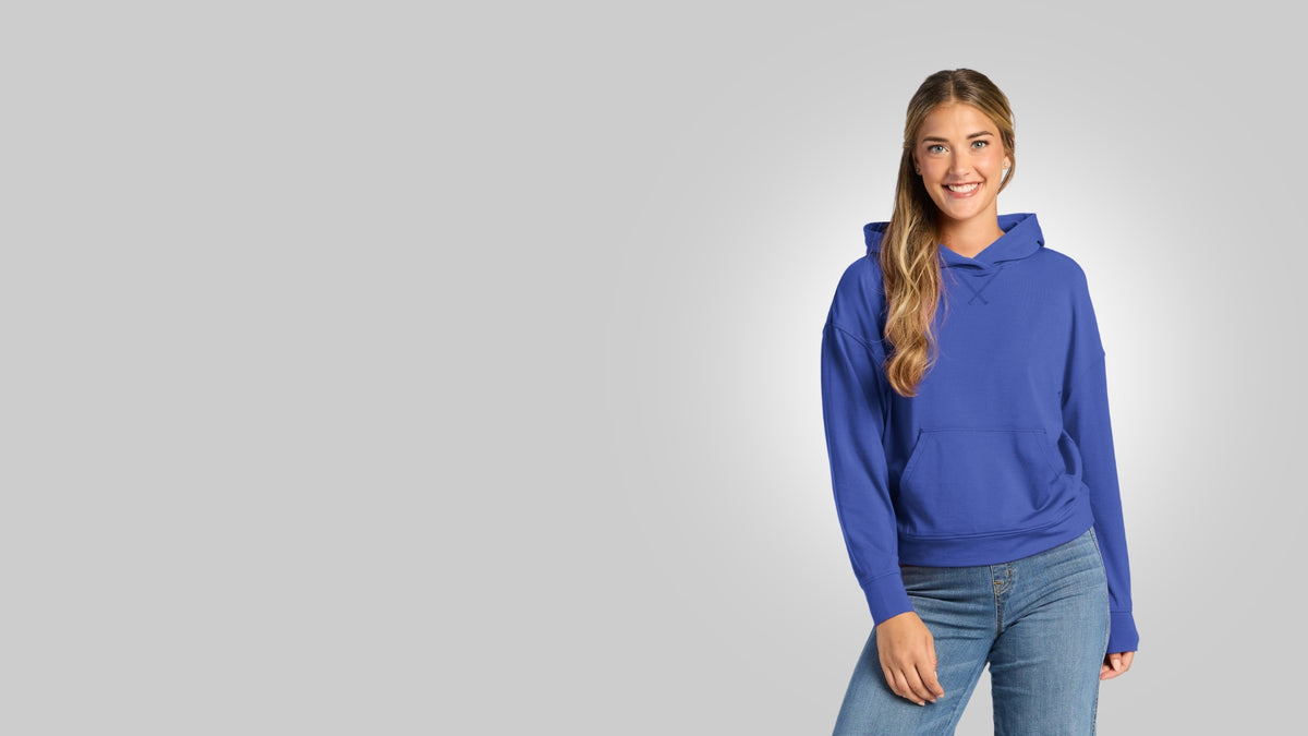 Smiling model wearing the Lizzy Hoodie in bright blue with light-wash jeans against a light gray background.