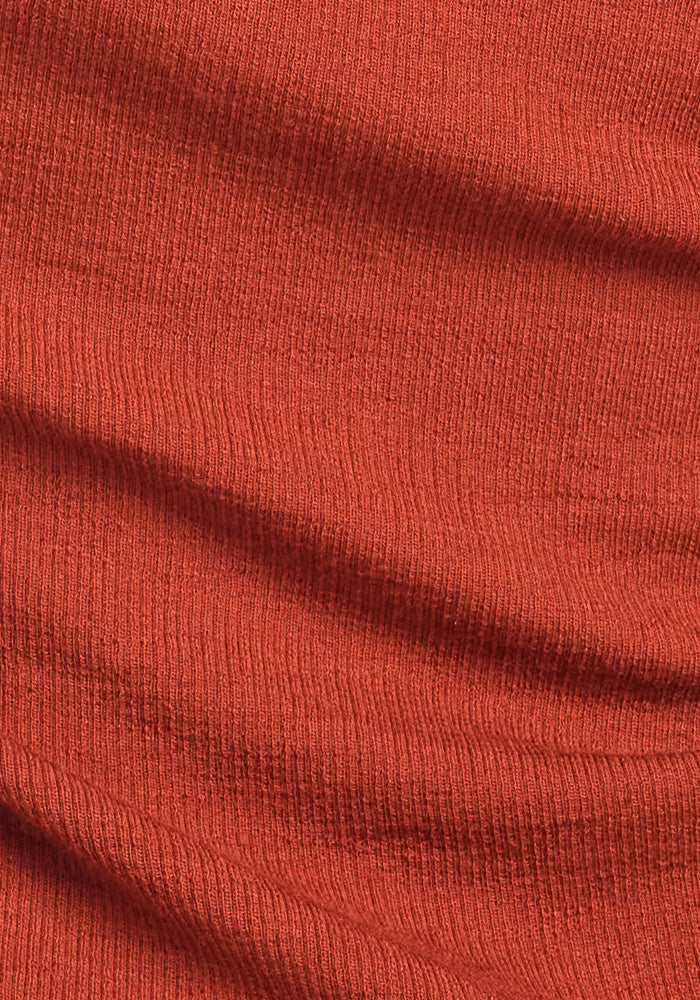A close-up of the Reese Ribbed Henley - Maple Leaf by Woolx shows its textured orange ribbed fabric with soft folds and a visible knit pattern, ideal for a warm winter shirt or cozy women’s top.