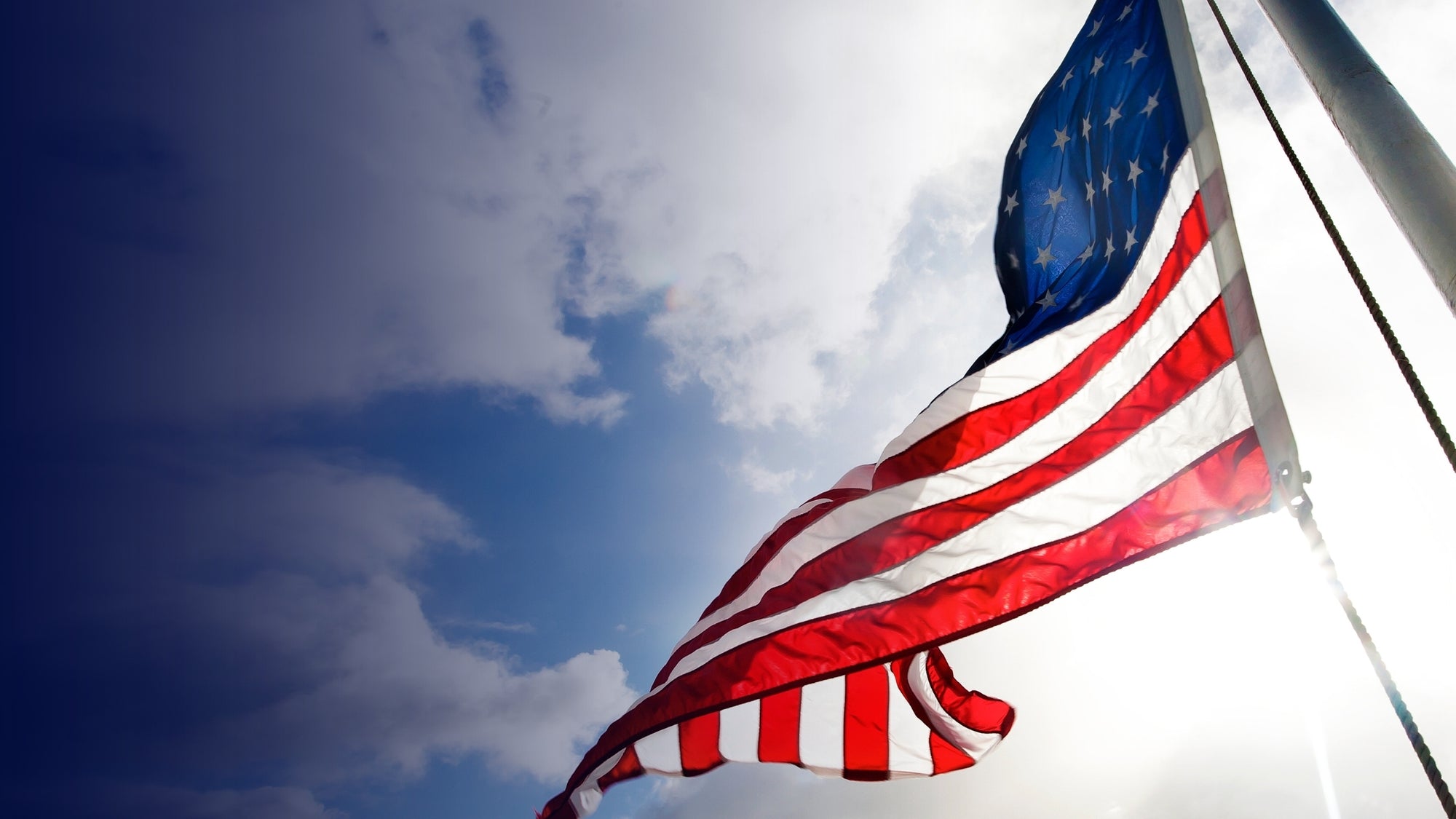 American flag waving against a blue sky with clouds