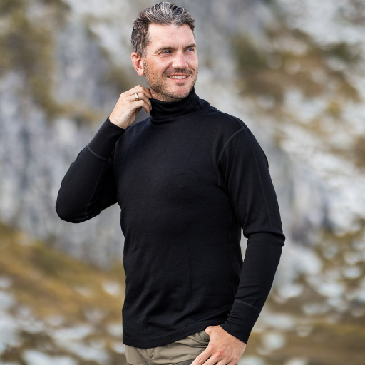A man wearing a black long-sleeve mock neck turtleneck sweater, standing outdoors against a blurred rocky mountain background.