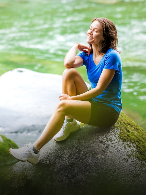 Woman sitting on a rock by a river, surrounded by nature