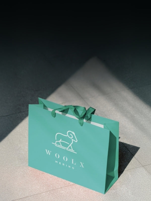 Green shopping bag with 'WOOLX' branding on a light surface.