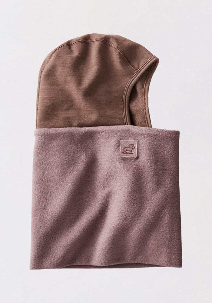 A folded Woolx Shellaclava in Plum Truffle with a small stitched logo, partially revealing a matching brown merino wool balaclava inside. Set against a plain, light background—perfect for cold-weather protection.