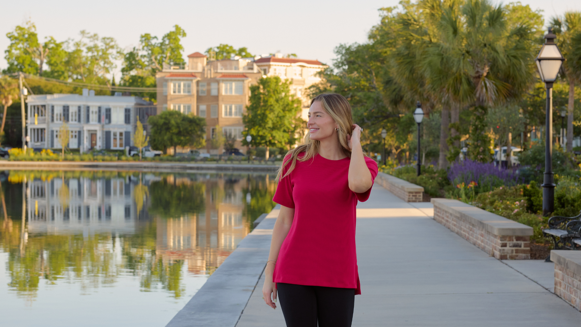 Woman in a red shirt walking on a sidewalk along the water. 