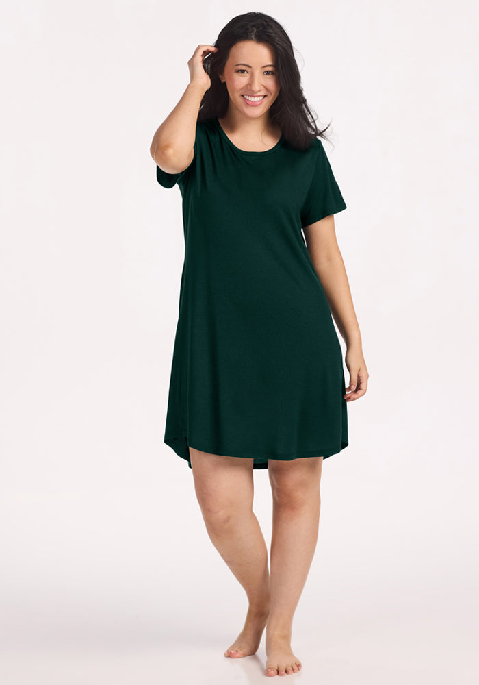 A person wearing a short-sleeved, deep pine Woolx Desi Nightgown in dark green merino wool with a round neckline. 