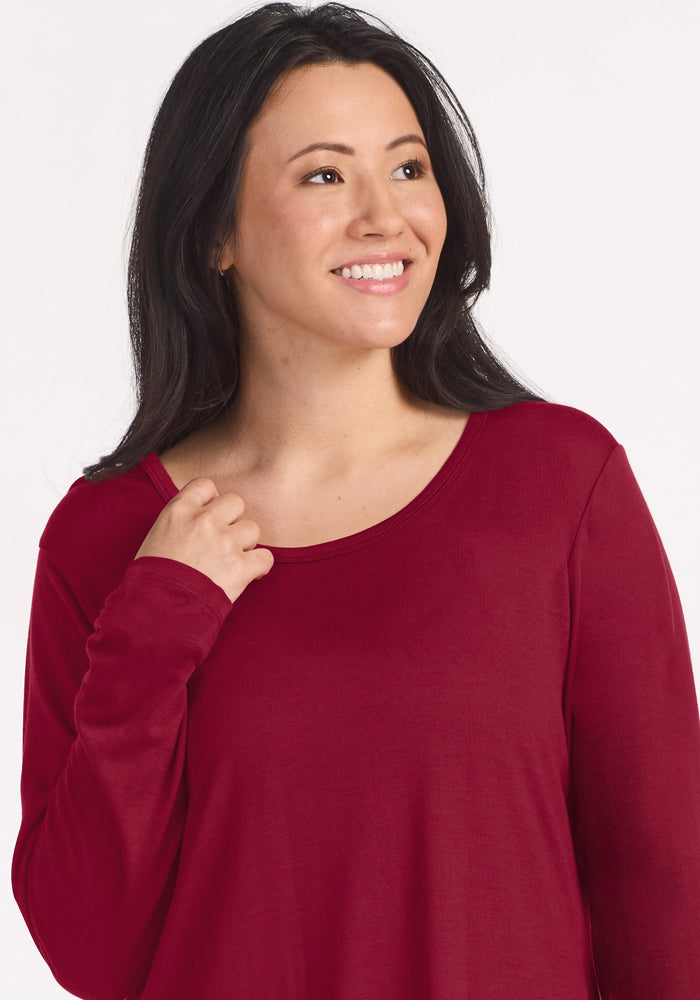 A woman smiles while wearing a red long-sleeved Woolx Lucille Long Sleeve Nightgown - Beet Red.