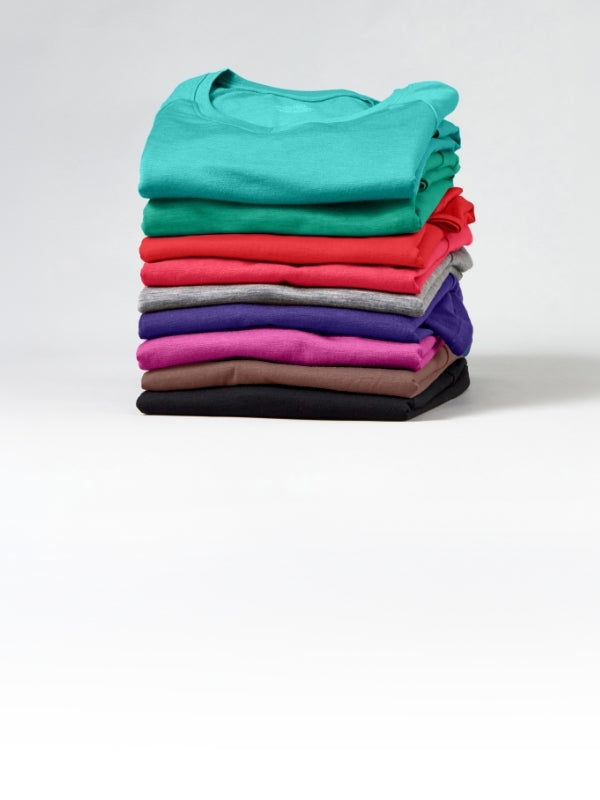 A stack of neatly folded short-sleeve t-shirts in multiple colors, including teal, green, red, pink, purple, gray, brown, and black, set against a plain light gray studio background.