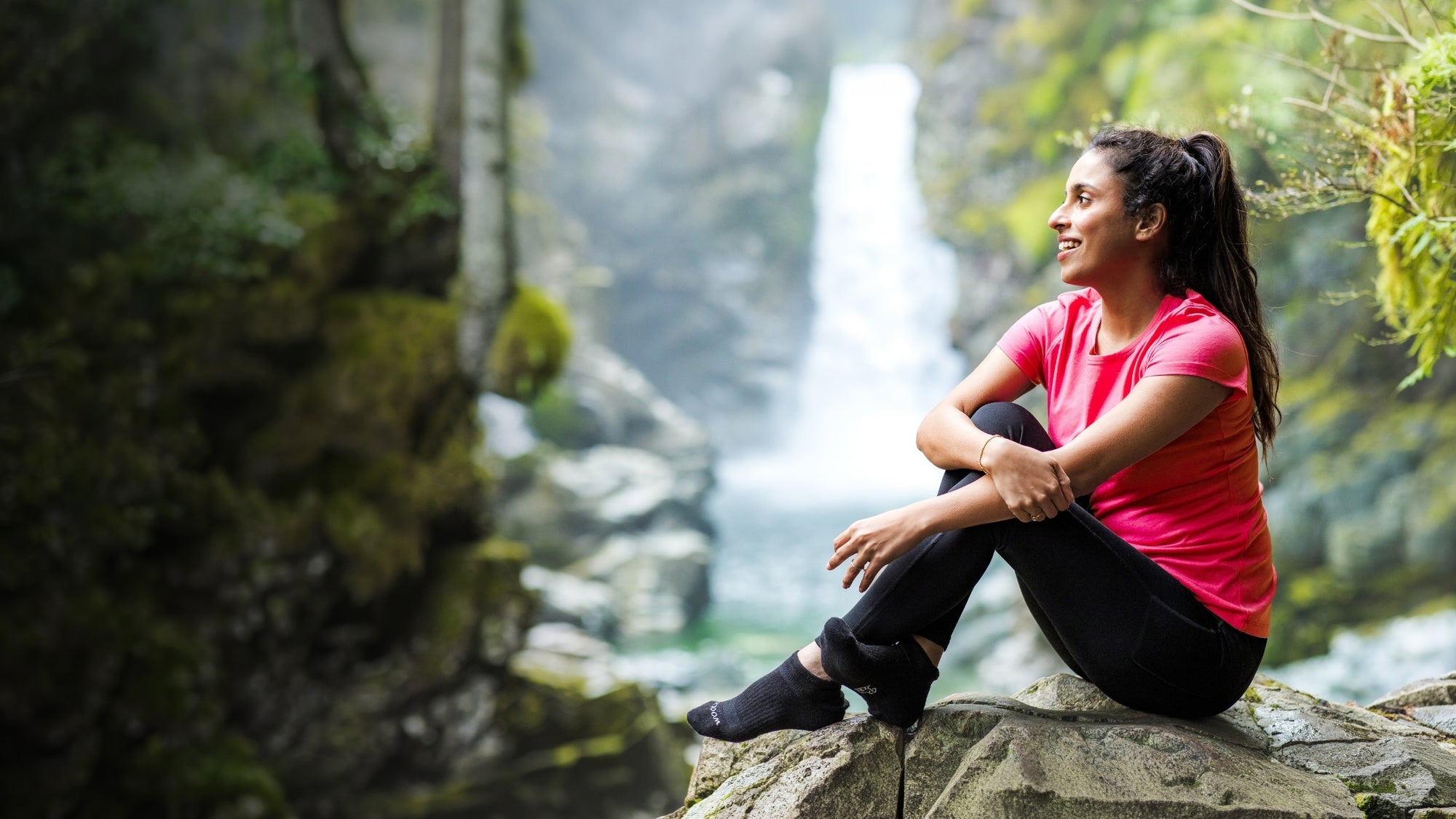 Woman sitting on a rock by a waterfall in a forest