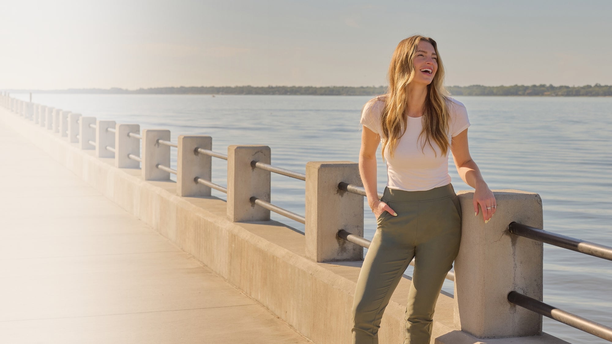Woman wearing a white t-shirt leaning against the railing of a pier and laughing. 