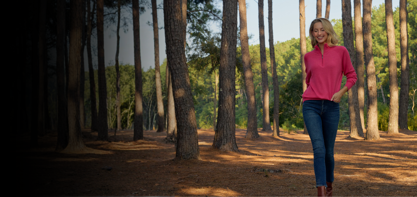 Woman standing in a forest wearing a pink sweater. 