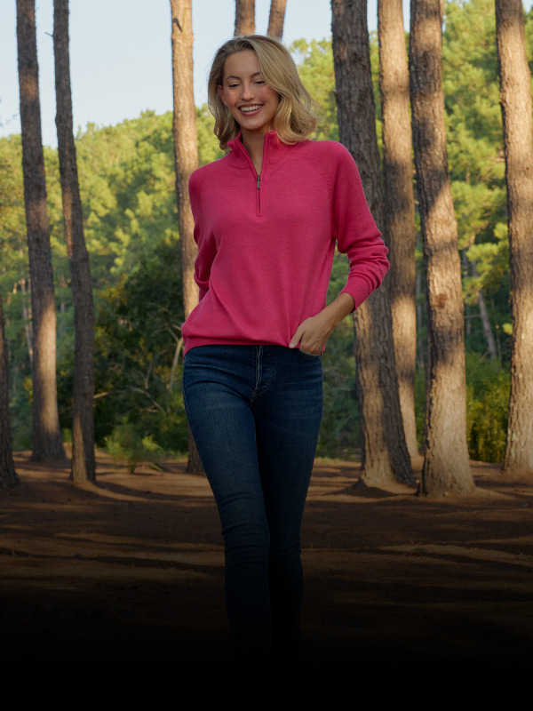 Woman standing in a forest wearing a pink sweater. 