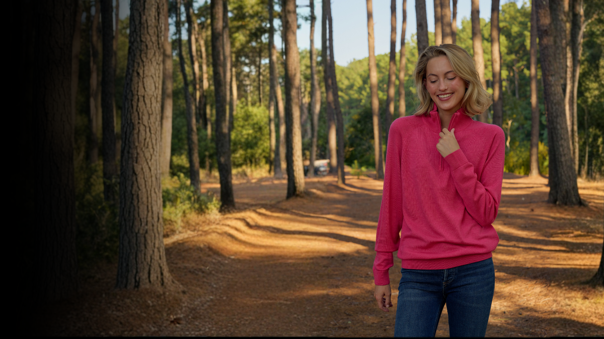 Woman standing in a forest wearing a pink sweater and smiling. 