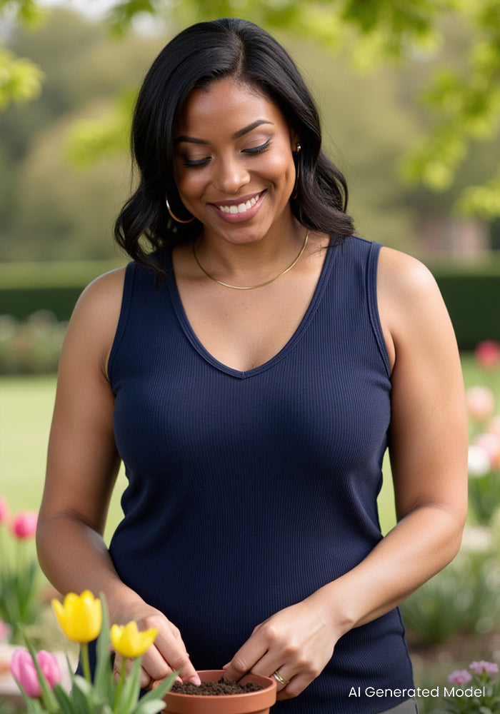A smiling woman in the Woolx Vivi Ribbed Tank in Deep Navy plants seeds among blooming tulips in a sunny garden.