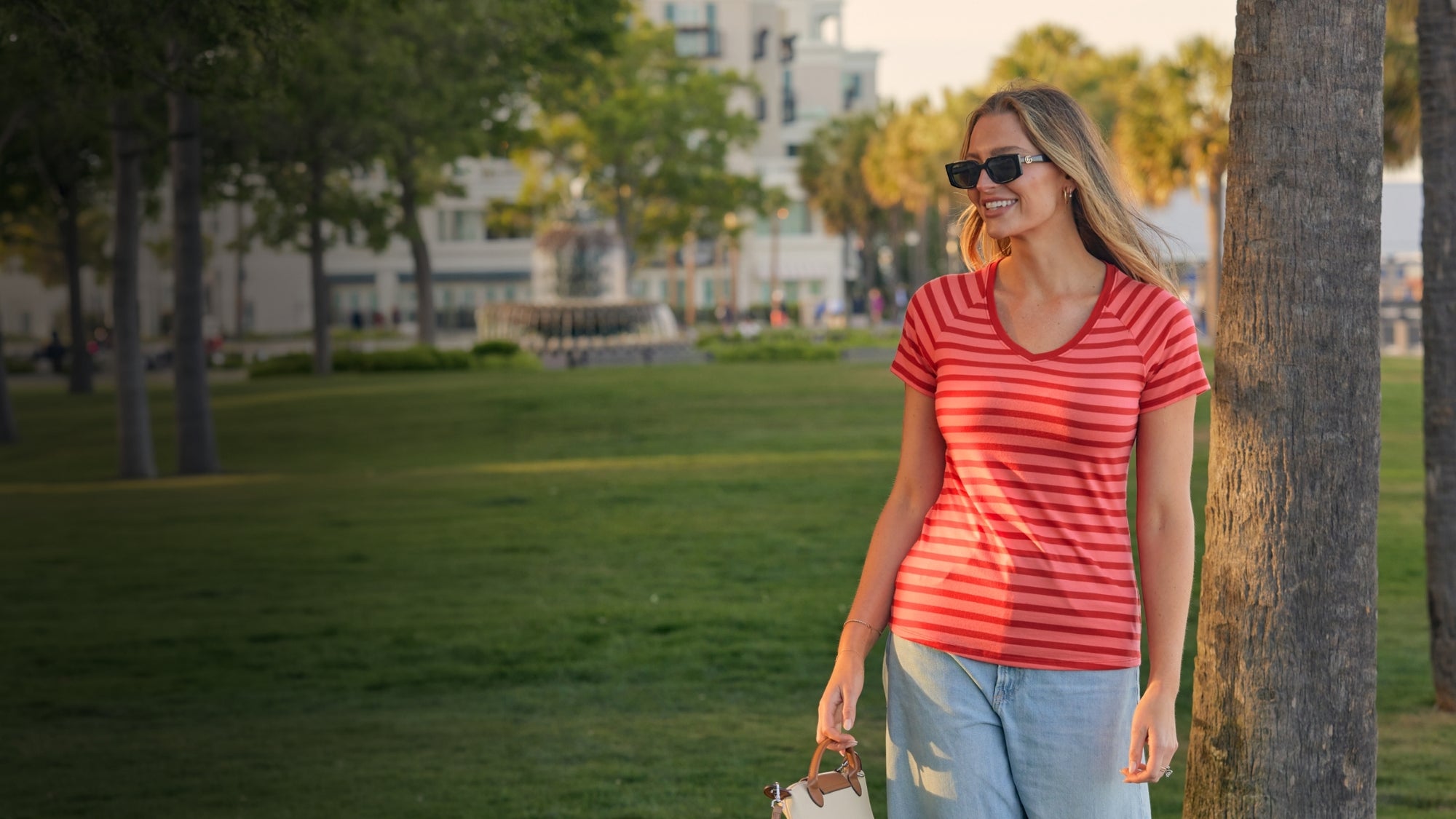 Woman in a red shirt and sunglasses walking in a park.