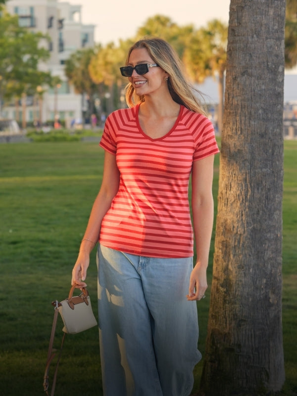 Woman in a red striped shirt and sunglasses standing next to a tree in a park.