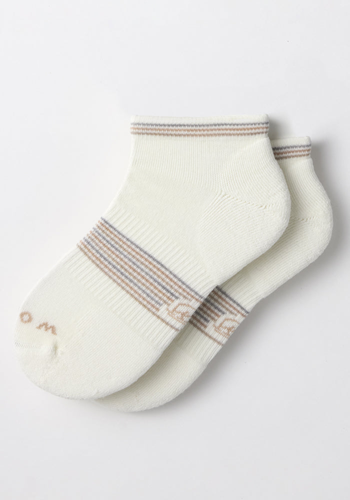 The Woolx Womens Amelia No Show Socks - White Lightning feature moisture-wicking fabric in white with beige and gray stripes at the top and near the toes, shown laid flat on a white background.